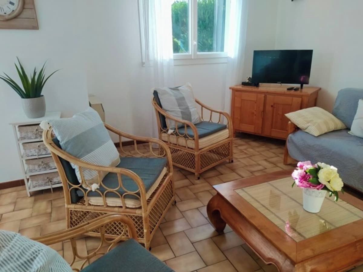 Un salon avec des fauteuils en osier, un canapé, une table basse et un téléviseur.