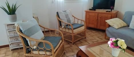 Een woonkamer met rieten stoelen, een bank, een salontafel en een televisie.