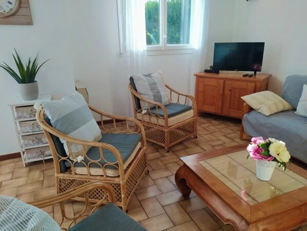 Uma sala de estar com cadeiras de vime, um sofá, uma mesa de centro e uma televisão.