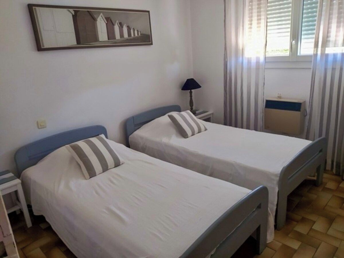 Habitació amb dos llits individuals, una taula de nit amb una làmpada, una finestra amb cortines i un mirall fixat a la paret.