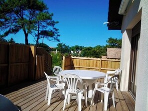 Un pati exterior amb una taula rodona i sis cadires, envoltat d'una terrassa de fusta i una tanca de fusta.