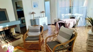 Un salon avec des meubles en osier, un coin repas avec une table et des chaises, et une cuisine à l’arrière-plan.