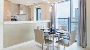 A modern kitchen with a built-in island, dining area with chairs and table, and large windows with curtains. - Manzil - High Floor 1BR in Business Bay (Dubai)
