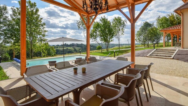 Ein überdachter Außenbereich mit Pool, Holz-Pergola und Gartenmöbeln.