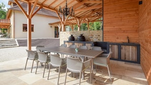 Eine Terrasse im Freien mit Holztisch und -stühlen, einer Steinmauer und einem eingebauten Grill.
