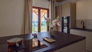 Eine Küche mit großem Fenster, einer Blumenvase, einem Topf auf dem Herd und einem Spülbecken.