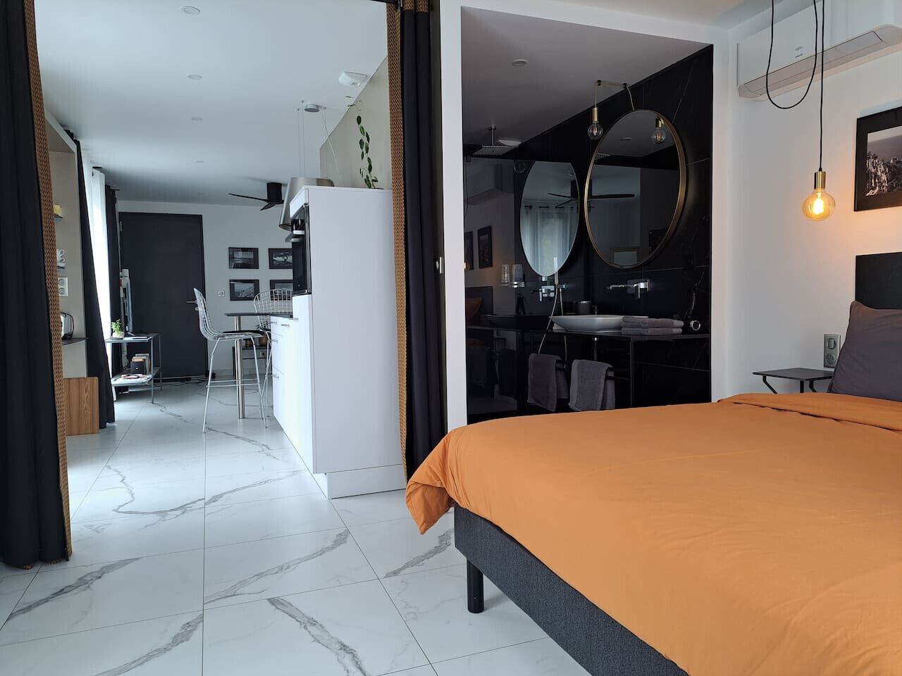 Et moderne hotelværelse med en stor seng, et badeværelse med et rundt spejl og et tekøkken.