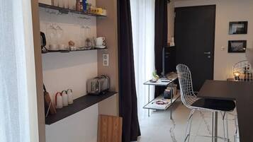 A compact kitchen with a dining area, featuring a built-in shelf with kitchenware, a black curtain, and a modern chair.