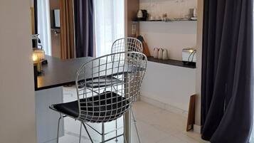 A modern kitchen with a dining area, featuring a metal wire chair, a small table, and a shelf with kitchen items.
