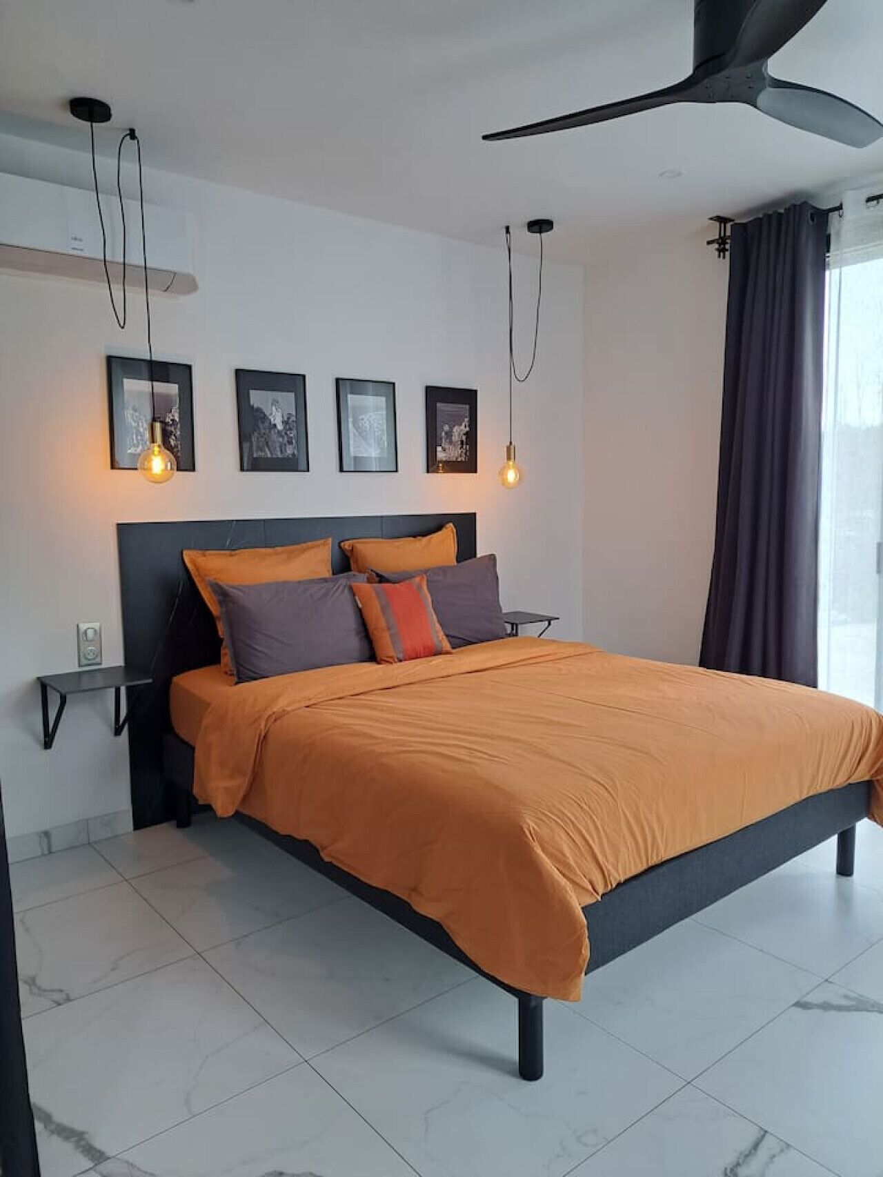 Een moderne slaapkamer met een groot bed, een plafondventilator en ingelijste foto’s aan de muur.