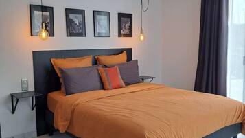 Een moderne slaapkamer met een groot bed, een plafondventilator en ingelijste foto’s aan de muur.