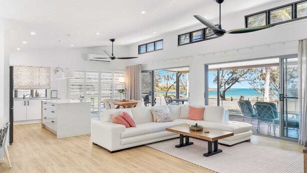 A spacious living area with a white sofa, a coffee table, and a view of the beach through large windows. - Luxury beachfront escape: Ocean views and poolside living! (Grasstree Beach)