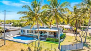A modern house with a swimming pool, surrounded by palm trees and a fenced yard. - Luxury beachfront escape: Ocean views and poolside living! (Grasstree Beach)
