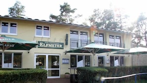 A building with a sign reading "ELFMETER" and outdoor umbrellas. - Pension Elfmeter (Rheinsberg)
