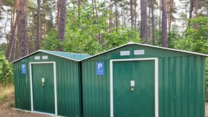 Two green portable cabins with white trim, each marked with a blue parking sign. - Pension Elfmeter (Rheinsberg)