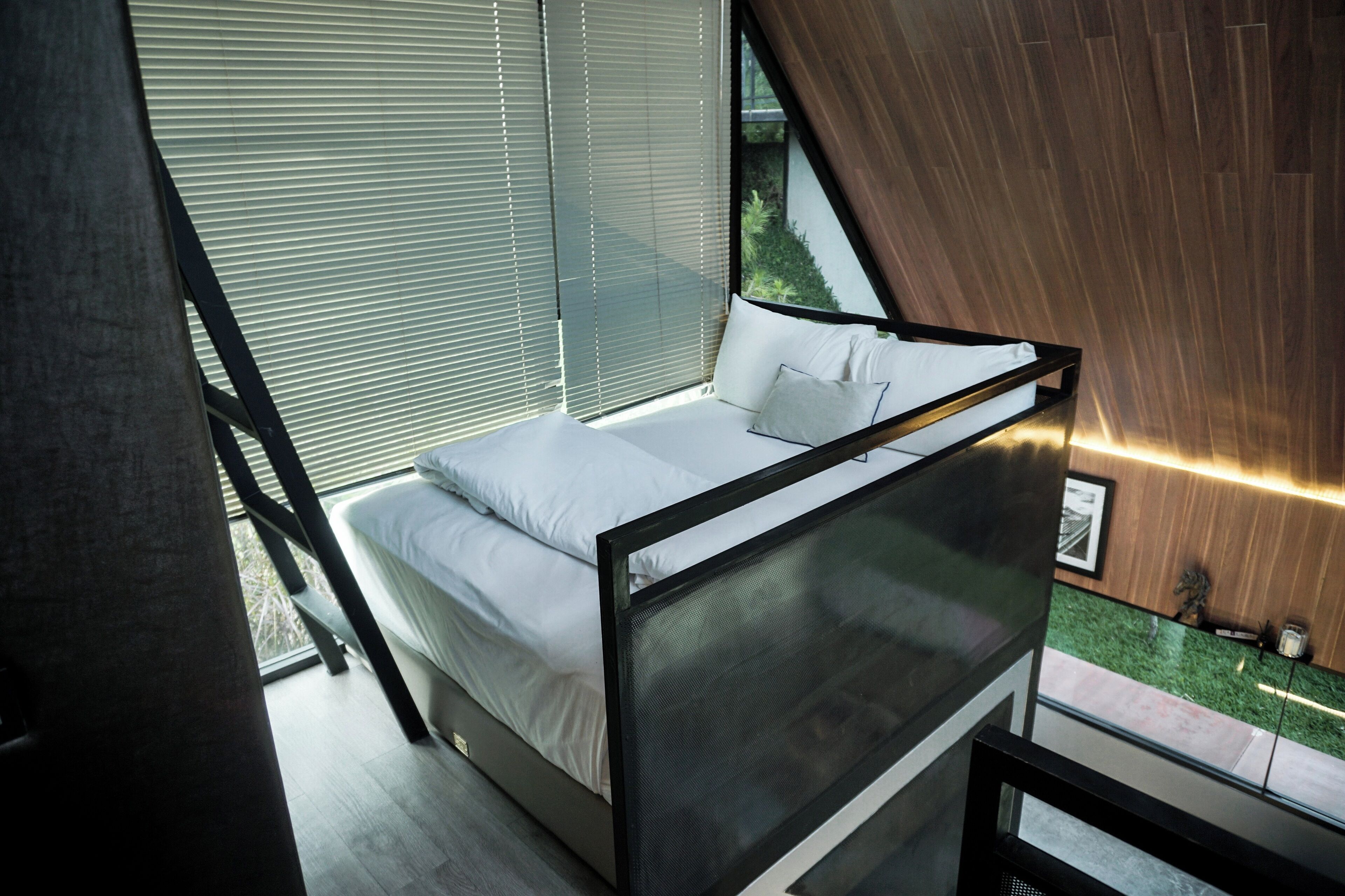 Un dormitorio moderno con cama, ventanas amplias y vistas a la vegetación.