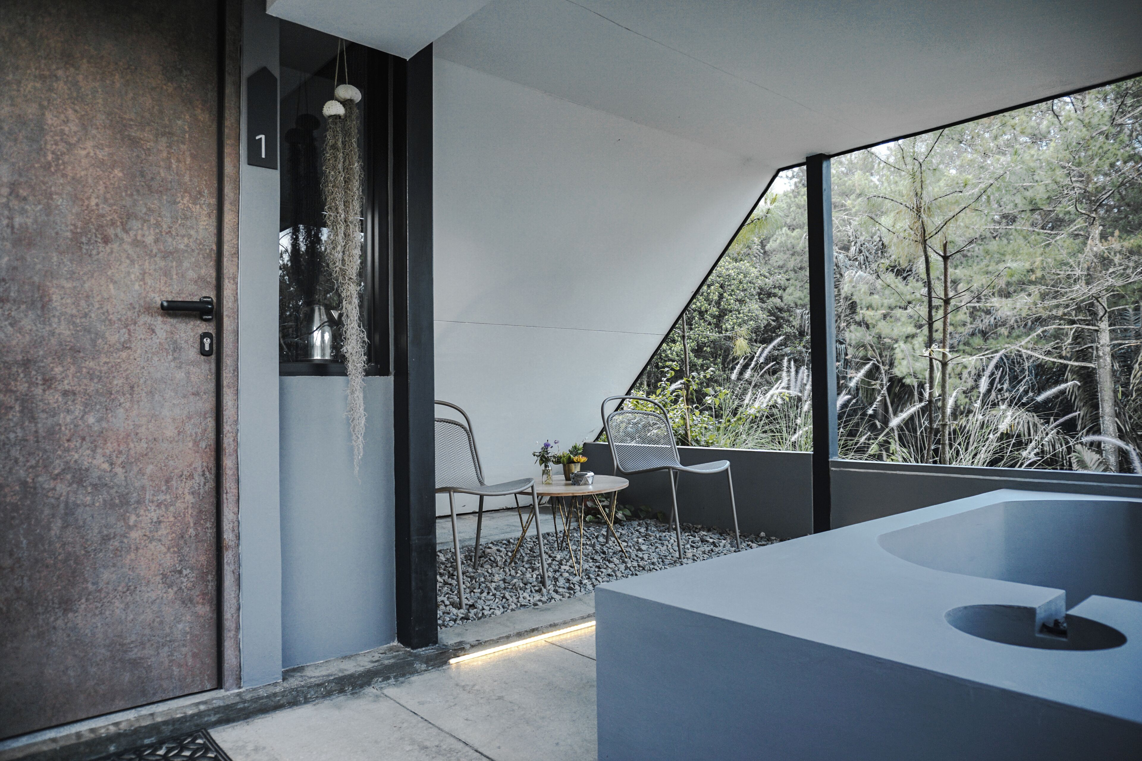 A modern bathroom with a large bathtub, a sink, and a window overlooking a garden.