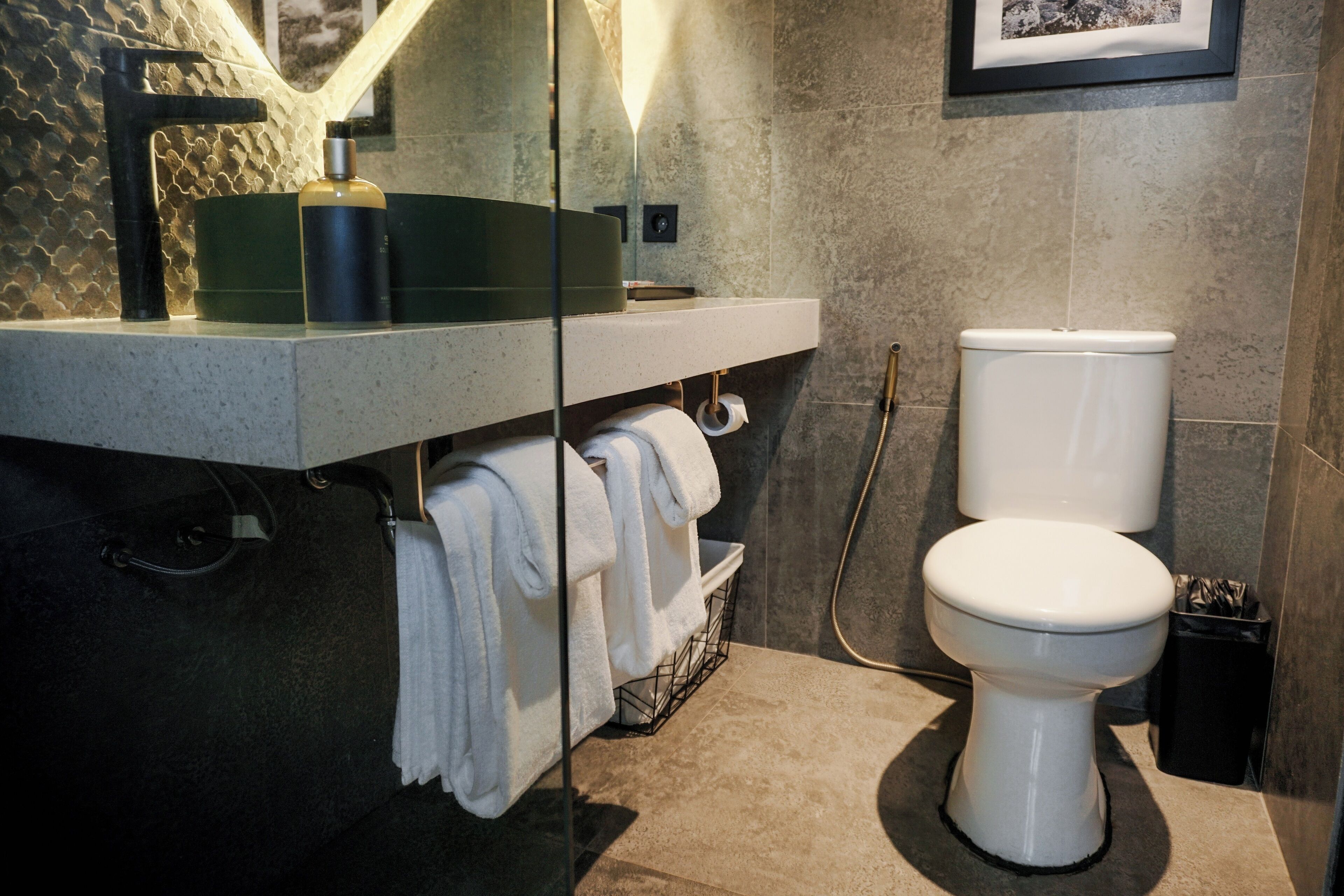 A modern bathroom with a glass-enclosed sink, a toilet, and a towel rack.