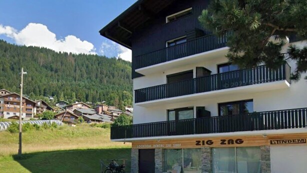 Ein mehrstöckiges Hotel mit Balkonen, ein Schild für einen Skiort und eine Aussicht auf eine gebirgige Landschaft.