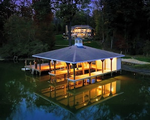 A floating house with a dock, a covered deck, and a large window overlooking a body of water.