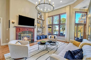 A living room with a fireplace, a television, and a large window with a view of trees.