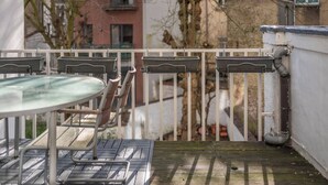 A balcony with a glass table and chairs, a metal railing, and a view of buildings and trees. - Room-euro Edens Brussels - Cozy Family S (Brussels)