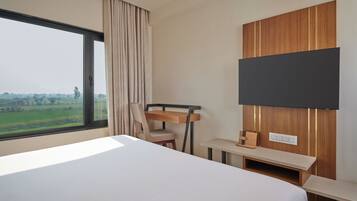 A hotel room with a large bed, a desk, a chair, a TV mounted on the wall, and a window with a view of greenery.