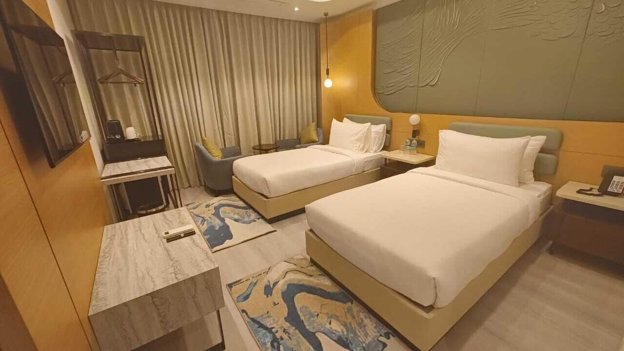 A hotel room with two beds, a desk, a chair, a small table, and a mirror.