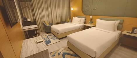 A hotel room with two beds, a desk, a chair, a small table, and a mirror.