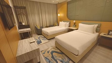 Habitación de hotel con dos camas, un escritorio, una silla, una mesita y un espejo.