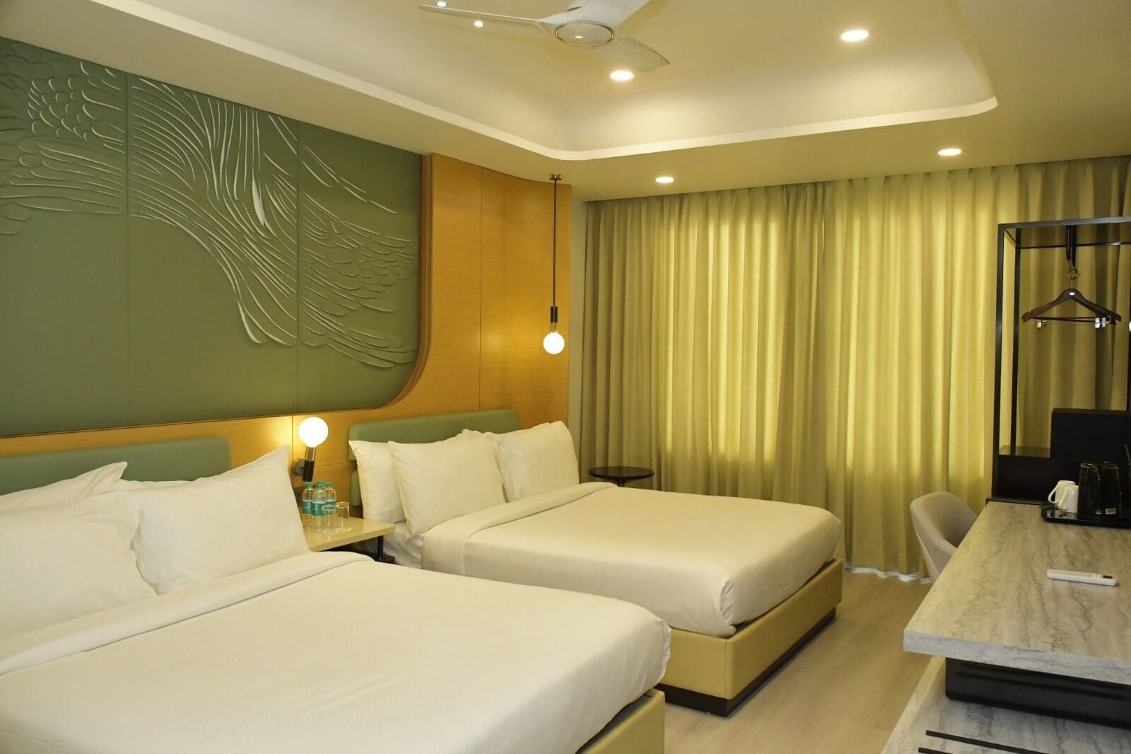 A hotel room with two beds, a desk, a chair, a small table, and a decorative wall panel.