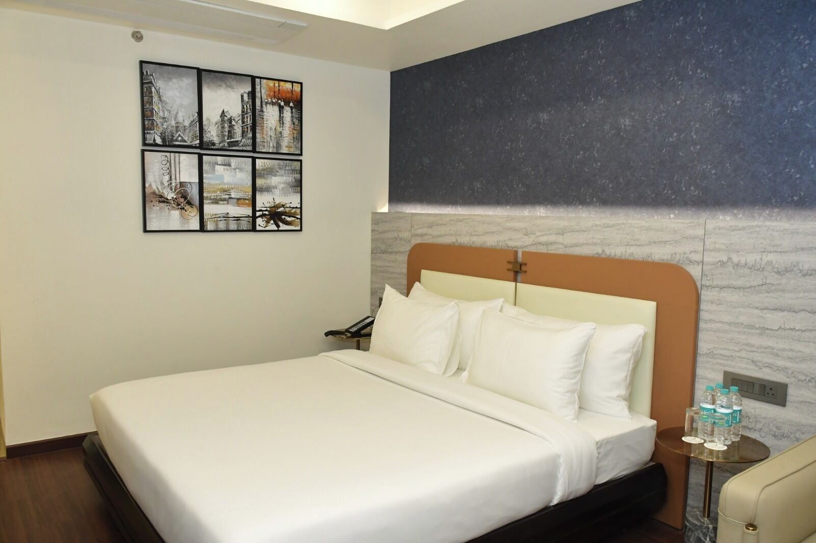 Habitación de hotel con una cama grande, cabecero con textura similar al mármol y una obra de arte en la pared que representa paisajes urbanos.
