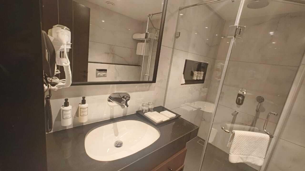 A modern bathroom with a large sink, a mirror, a glass shower enclosure, and a towel rack.
