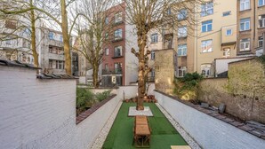 A courtyard with a wooden bench, a tree, and a green artificial turf. - Room-euro Edens Cosy Historic Home in Br (Brussels)