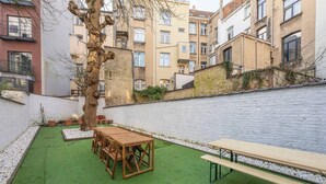 A courtyard with a wooden table and benches, surrounded by a white brick wall and a tree. - Room-euro Edens Cosy Historic Home in Br (Brussels)
