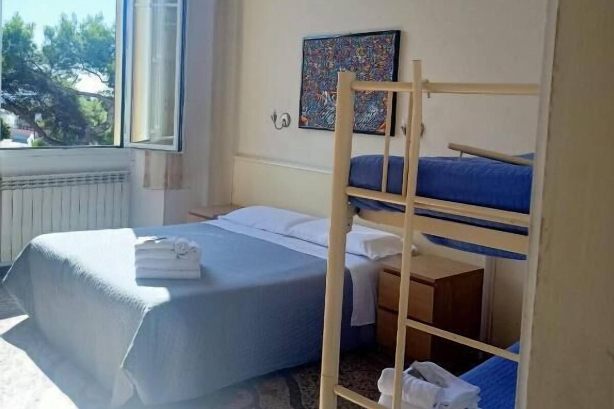 Una habitación con una cama litera, una cama individual y una ventana que da a un paisaje de árboles.