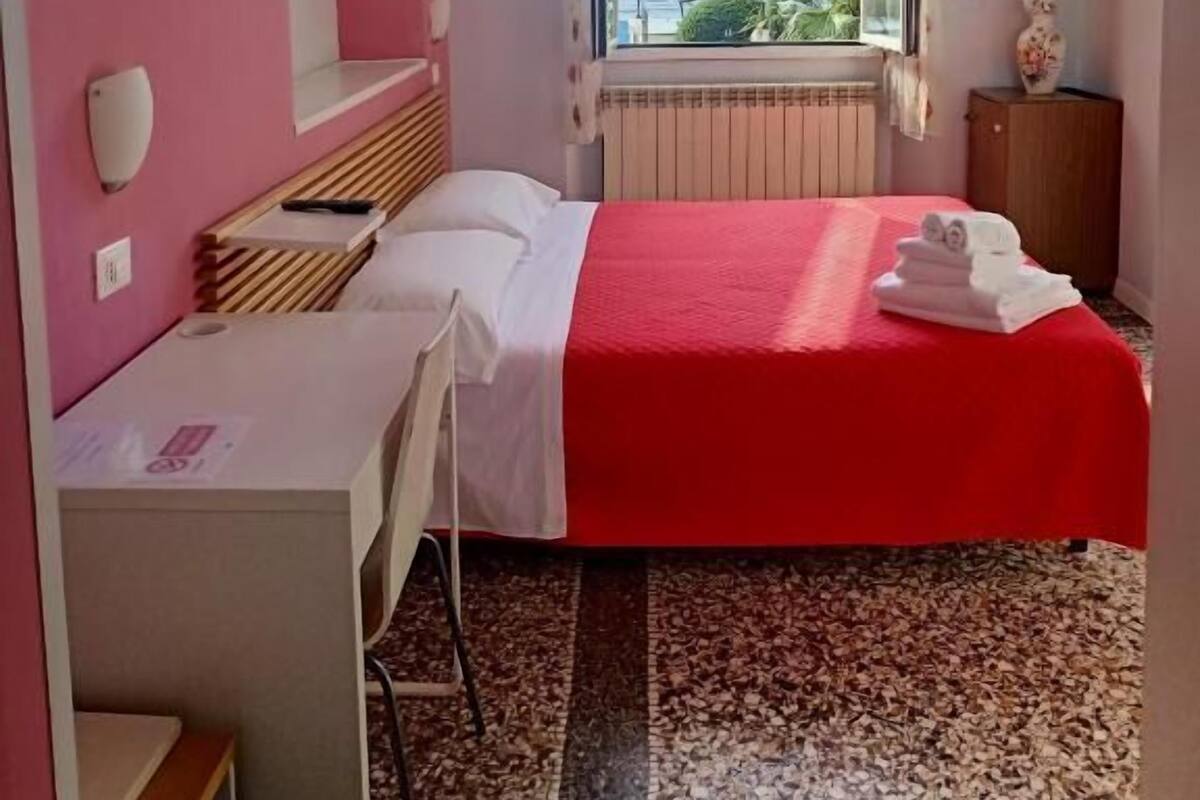 Habitación de hotel con cama, escritorio, silla, ventana con vistas y radiador.