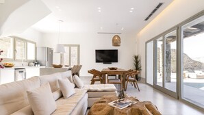 A modern living room with a sofa, coffee table, and dining area. - Denia Seaside Villa III,Private Heated Pool! (Mykonos)