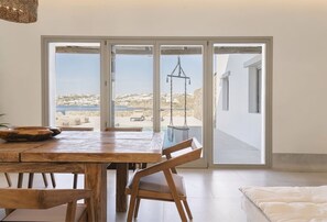 Un espace repas avec une table et des chaises en bois, un luminaire suspendu et une vue sur une terrasse extérieure, accessible par de grandes portes vitrées.