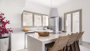 A modern kitchen with a central island, white cabinetry, and a stone wall backdrop. - Denia Seaside Villa III,Private Heated Pool! (Mykonos)