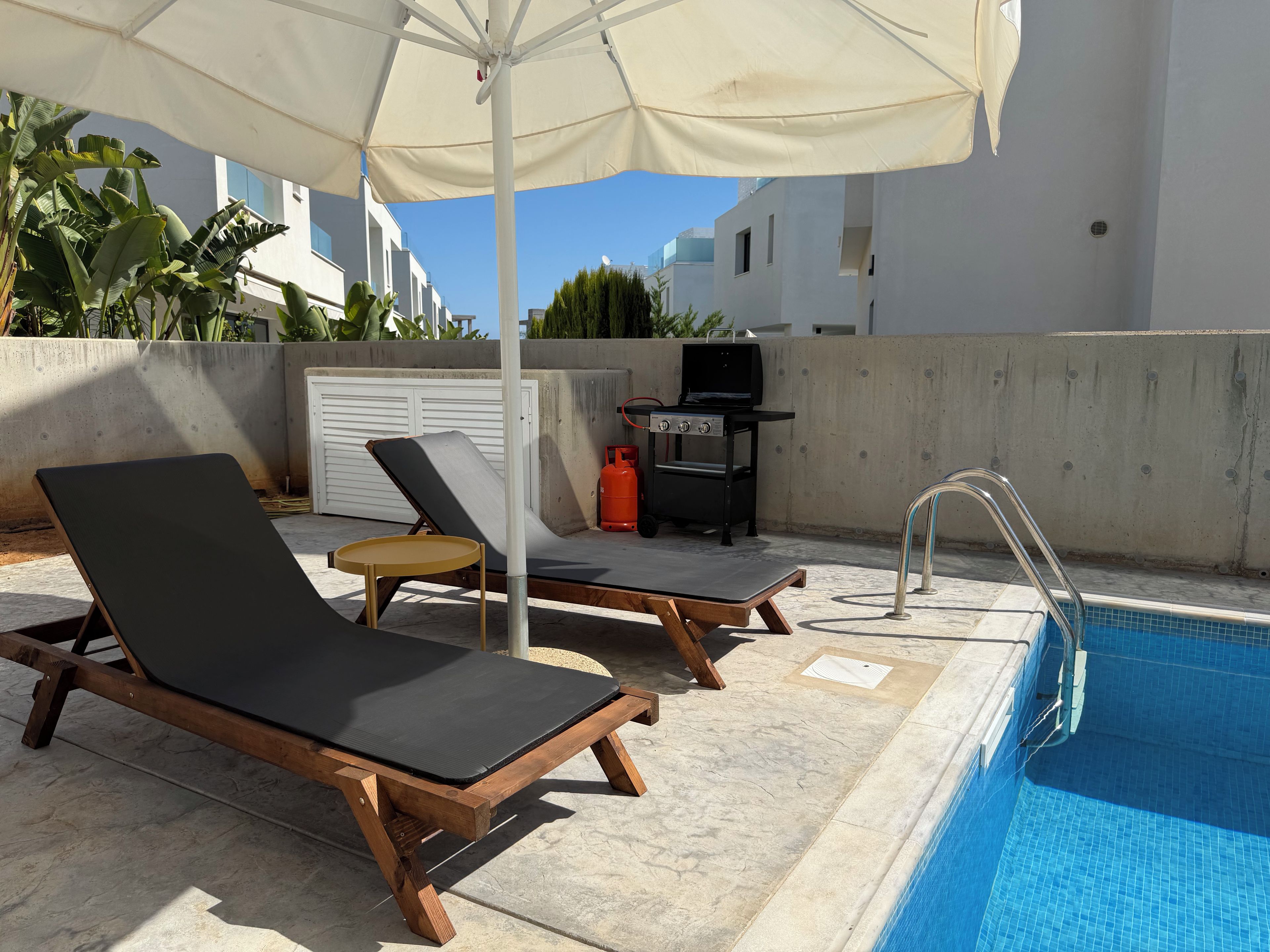 A poolside area with lounge chairs, a barbecue grill, and a pool.
