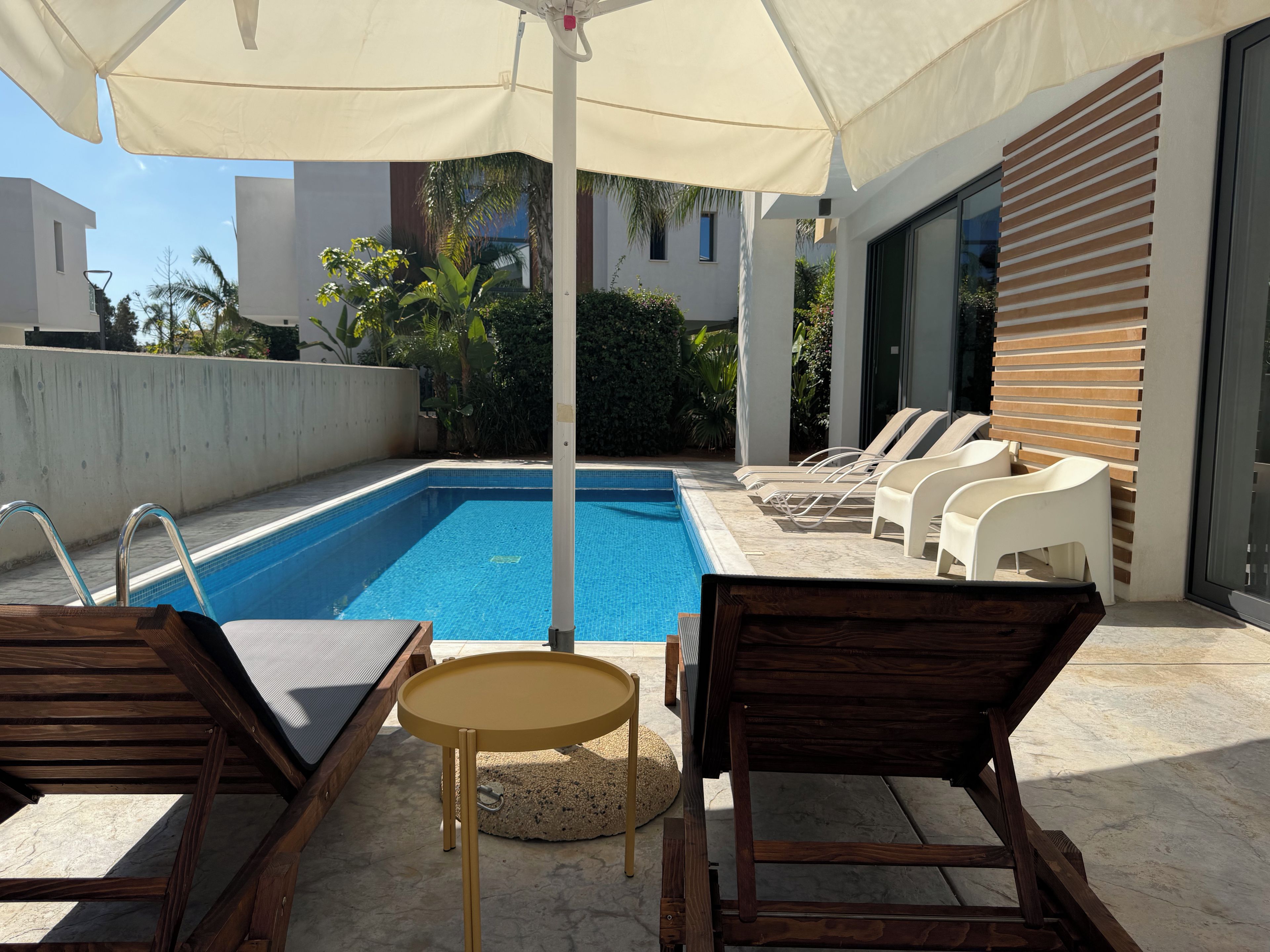 A swimming pool with lounge chairs and a table, surrounded by a covered patio area.