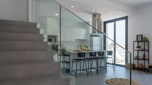 Une cuisine moderne avec un escalier en verre, un îlot central doté de tabourets de bar et une vue sur l’extérieur.