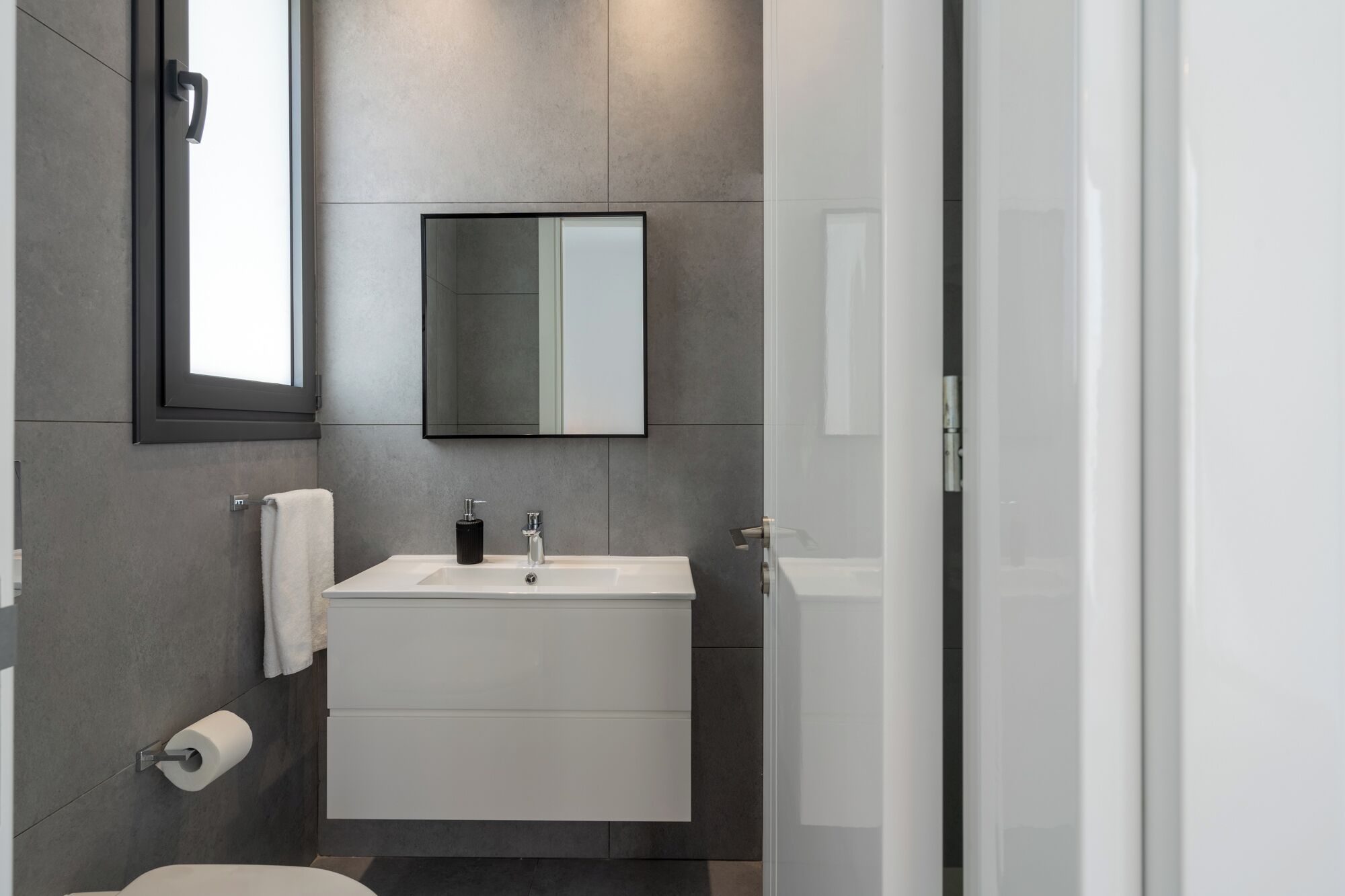 A modern bathroom with a white sink, a mirror, and a toilet.