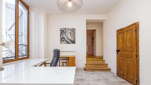 A modern kitchen with a white countertop, a chair, and a table. There is a wooden door and a staircase leading to another room. - Le Fare d'Emilie - Polynesian stopover (Gaillac)