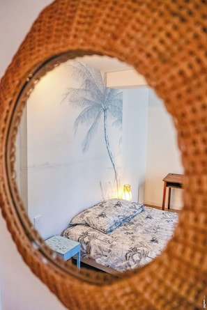 A room with a bed, a small table, a lamp, and a wall with a palm tree mural. - Le Fare d'Emilie - Polynesian stopover (Gaillac)