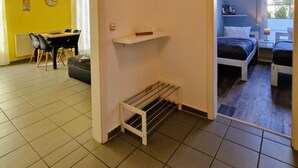 Una stanza compatta con un letto, uno scaffale piccolo, un'asta per stendere i panni e un'area pranzo con tavolo e sedie.