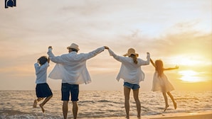 Une famille de quatre personnes se promène sur la plage au coucher du soleil, se tenant la main et regardant l’océan.