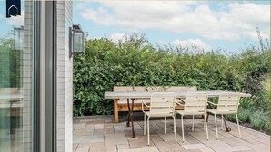 Une terrasse extérieure avec une table et des chaises en bois, un banc et une haie en arrière-plan.