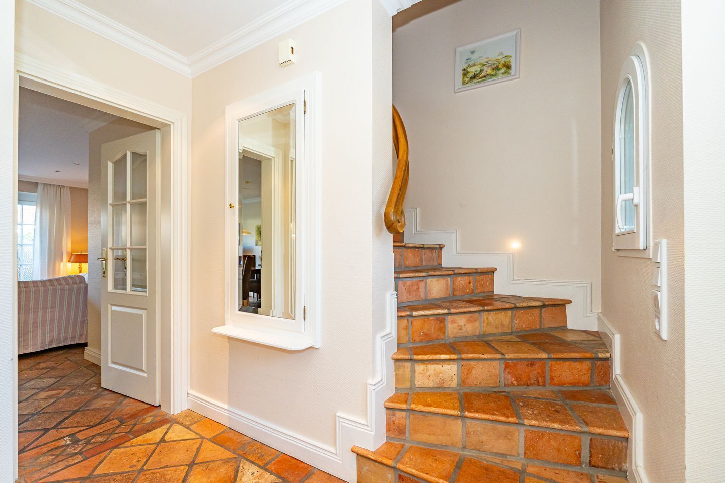 Una escalera con baldosas de terracota, una puerta con un espejo y un cuadro en la pared.
